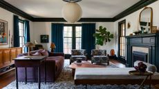 Living room with green ceiling trim, large windows with blue drapes, a large fireplace with a boat on the mantel, a purple sofa, a chaise lounge, and two floral armchairs, with a lantern light above.