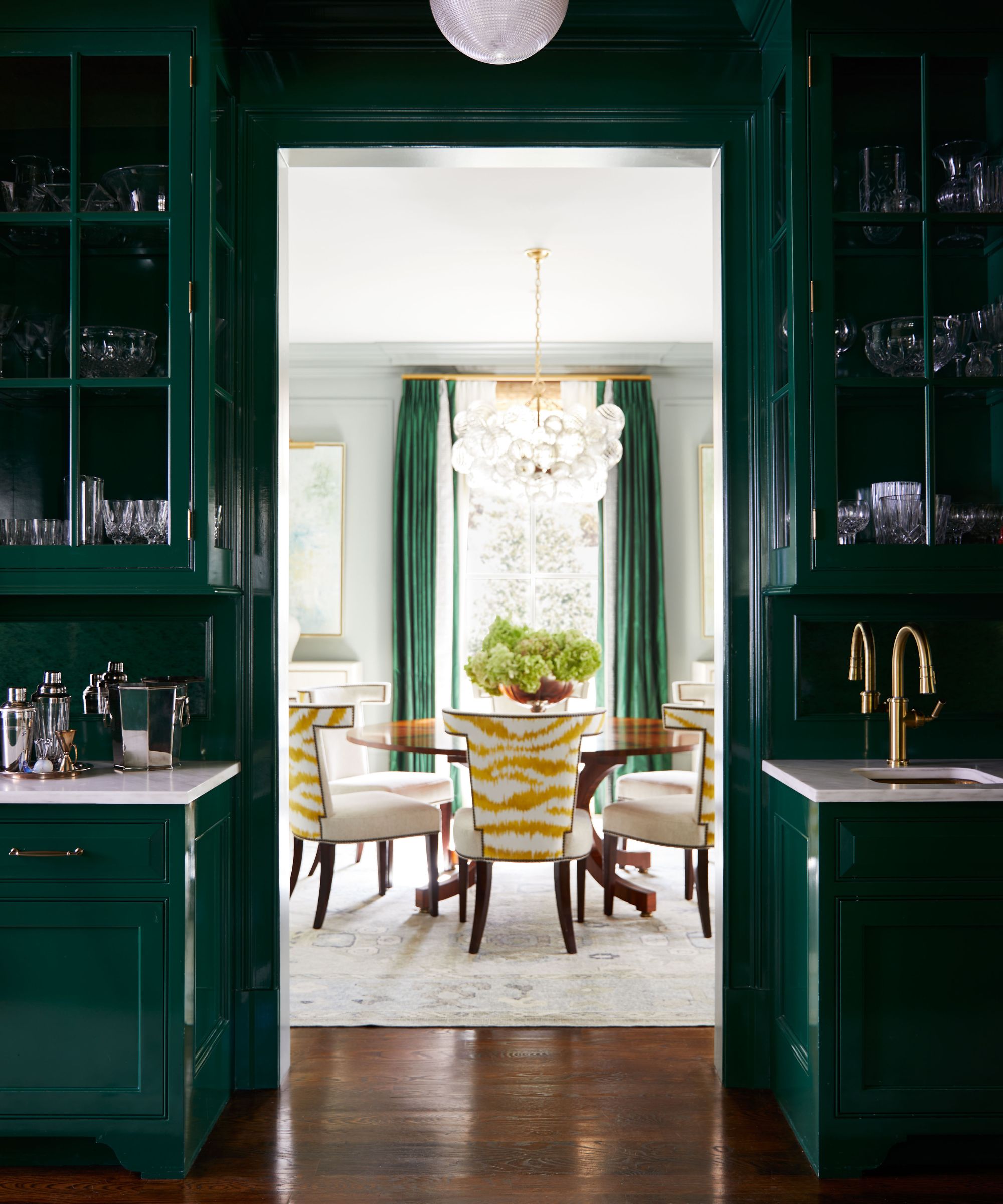 A dark green pantry room in a gloss sheen, leading into a white dining room.