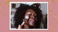 A woman with curly hair and glowing skin is pictured applying highlighter to her cheekbone with a fluffy brush/ in a pink and gold glitter template