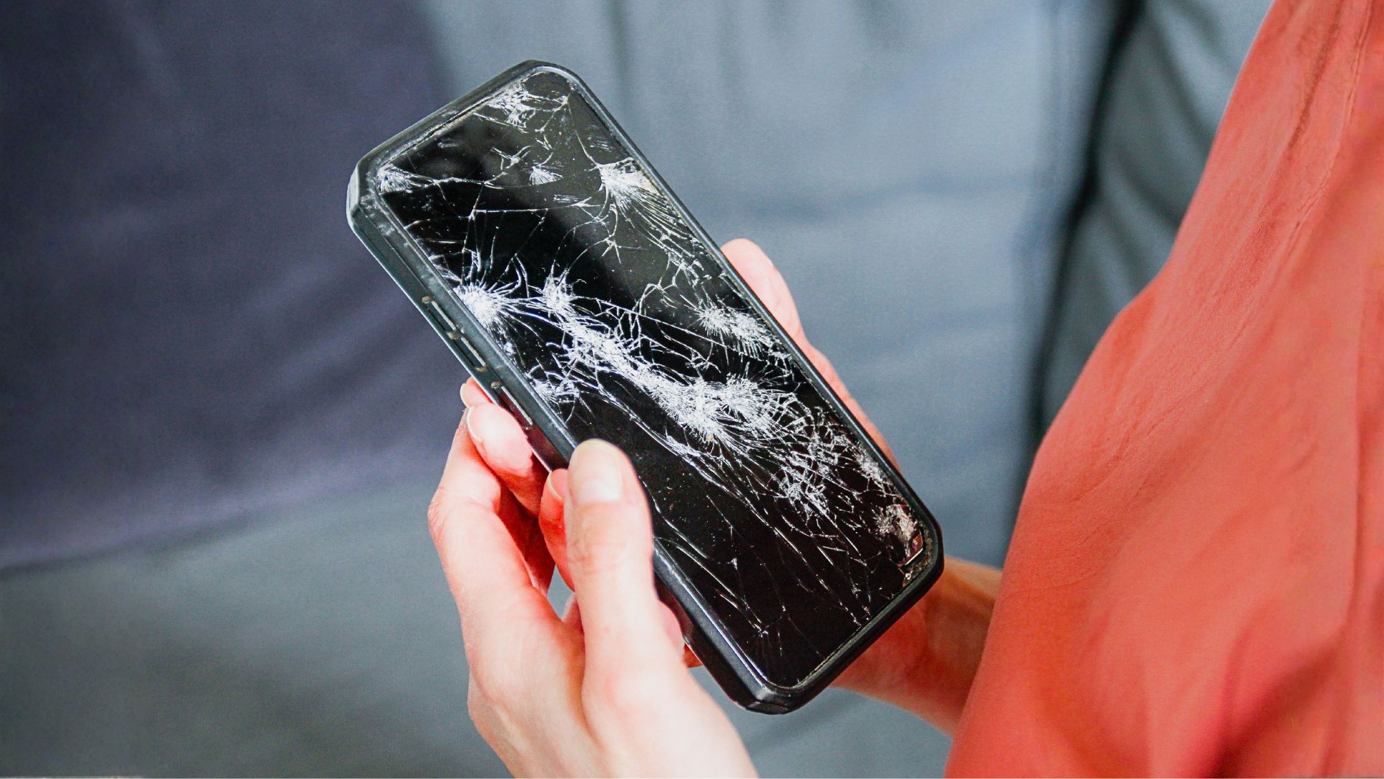 A person holding a smartphone with a cracked screen. 