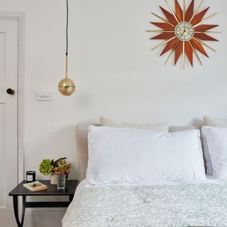 Bedroom with bedding in neutral colours and a retro sunburst style clock