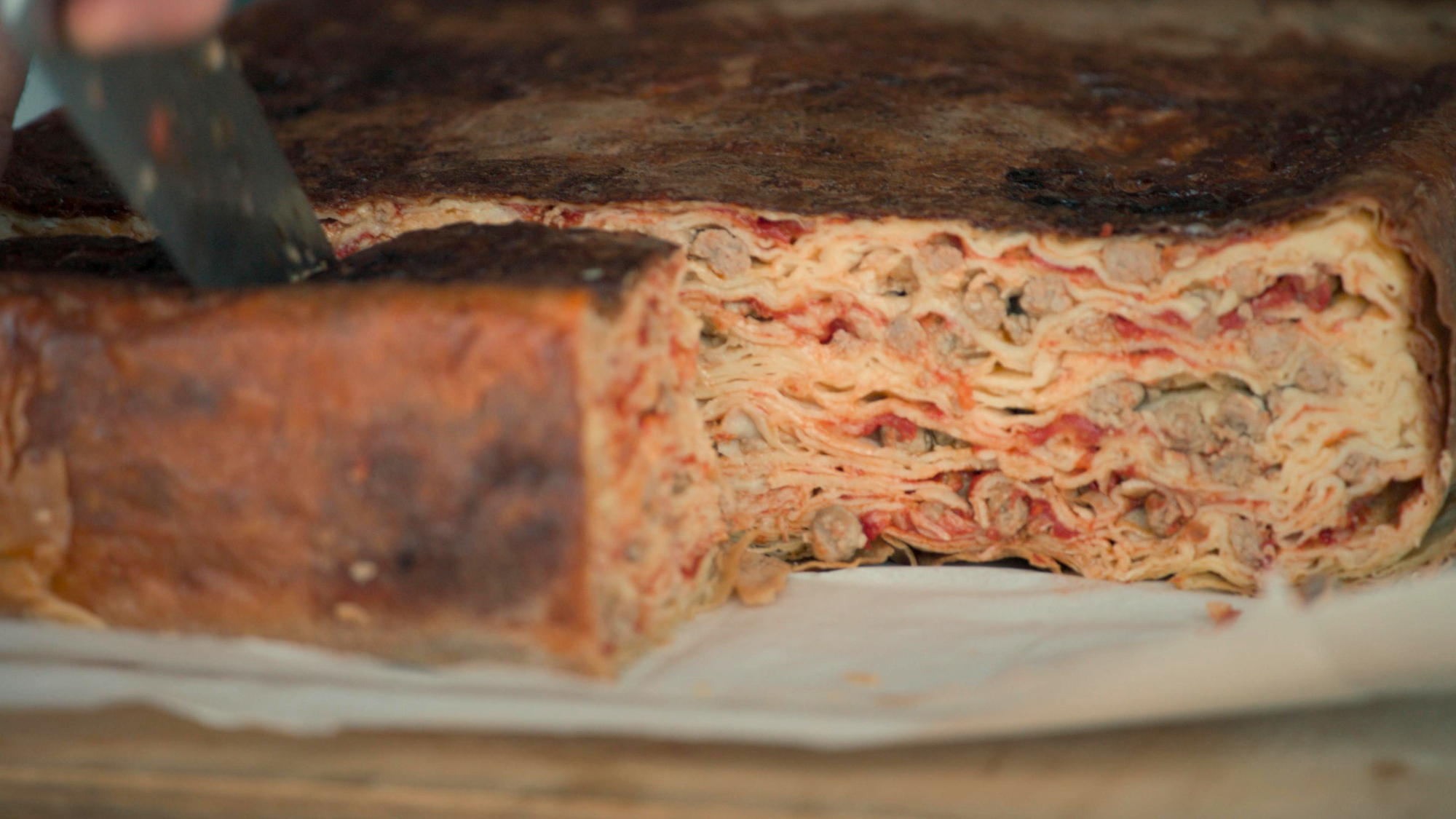 Timballo being cut, revealing the intricate layers of crespelle and meatballs inside.