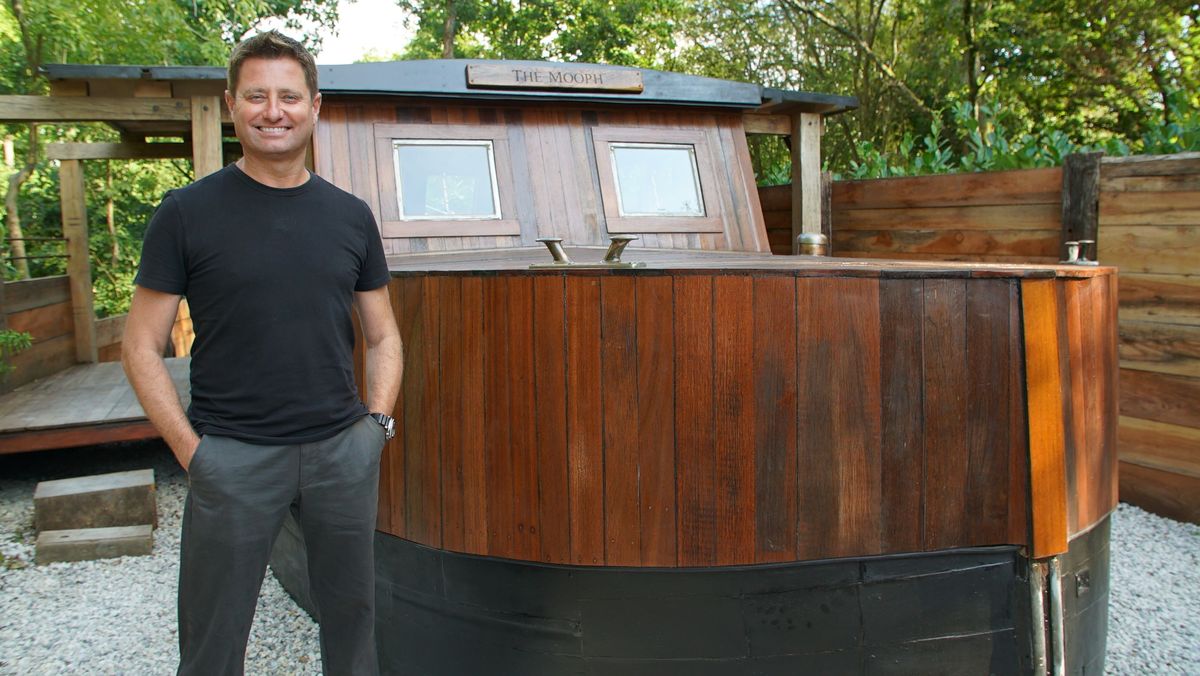 George Clarke standing in front of a wooden boat