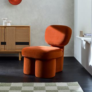 Orange velvet chunky leg chair on a black floor with rustic grey walls behind