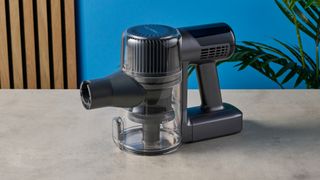 a modern-looking sleek shiny vacuum cleaner with light grey components on a carpet in front of a blue background