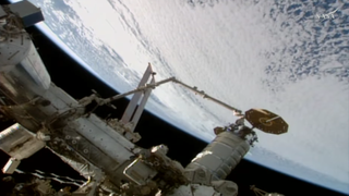a spacecraft is held by a robot arm over Earth