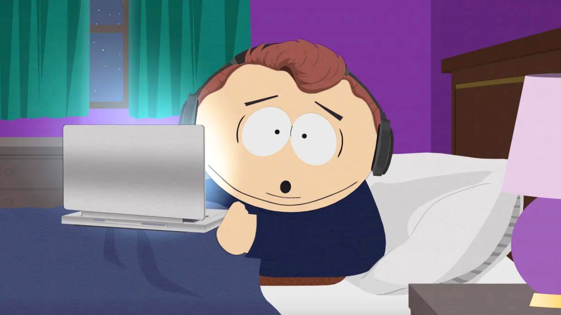 A boy looks shocked holding a laptop in bed while wearing headphones