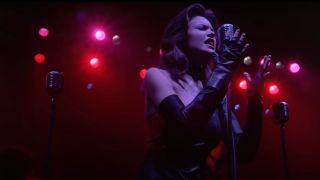 Diane Lane sings in front of a microphone on a red lit stage in Streets of Fire.