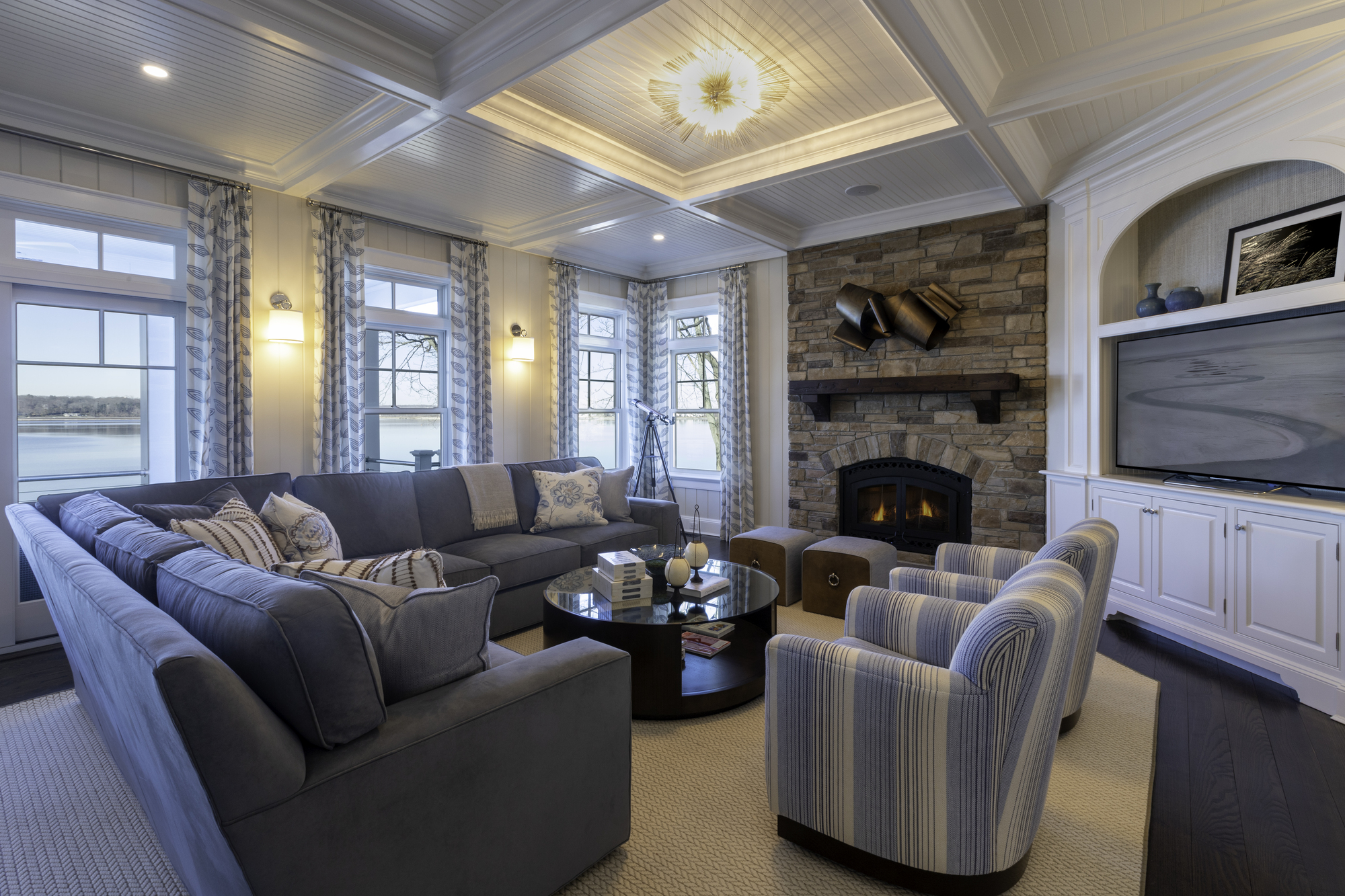 A coastal style living room with a blue sofa, blue and white striped arm chairs, and a corner media unit with a TV