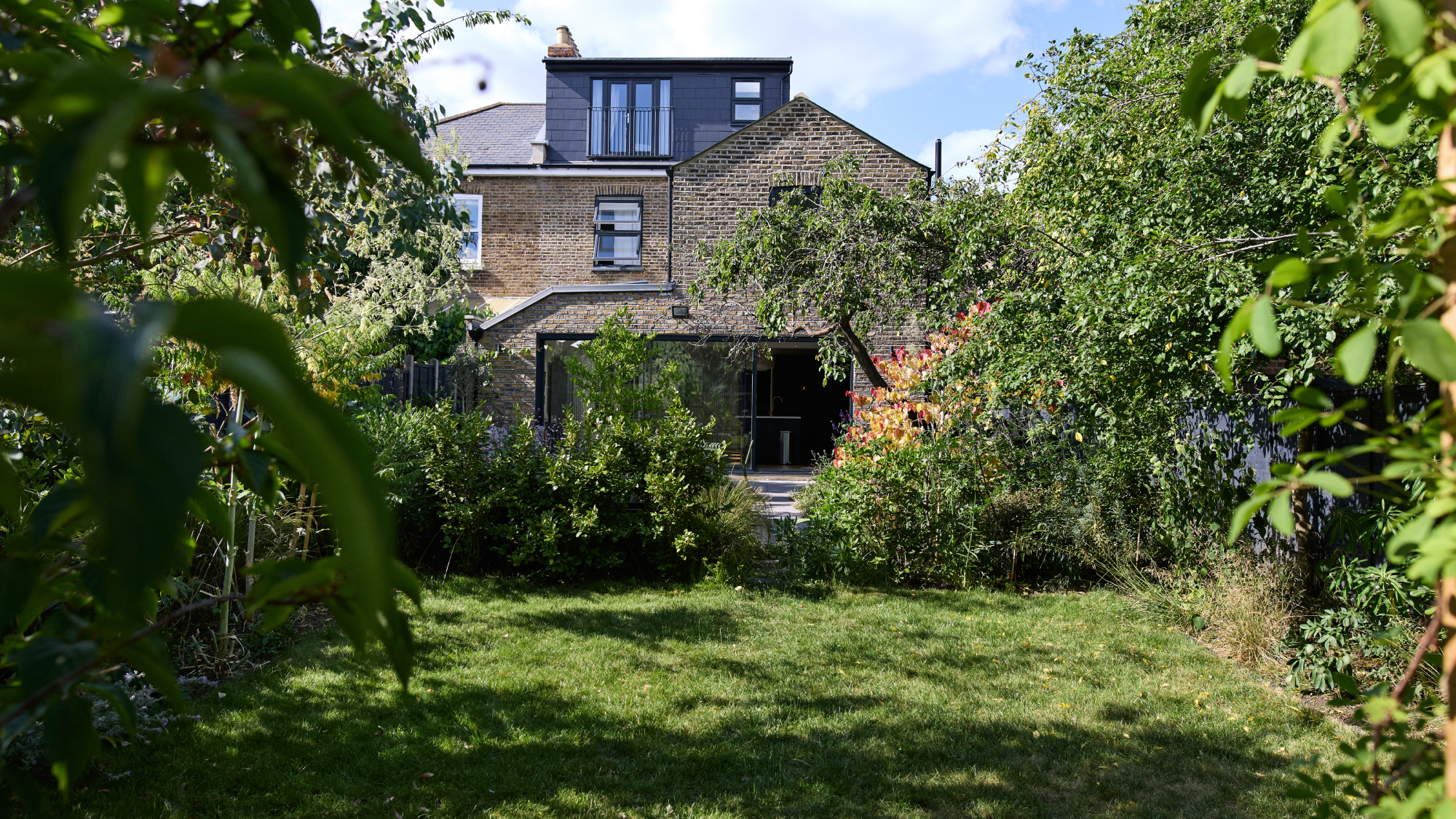 overgrown garden with lawn, trees and house in distance with extension and loft conversion