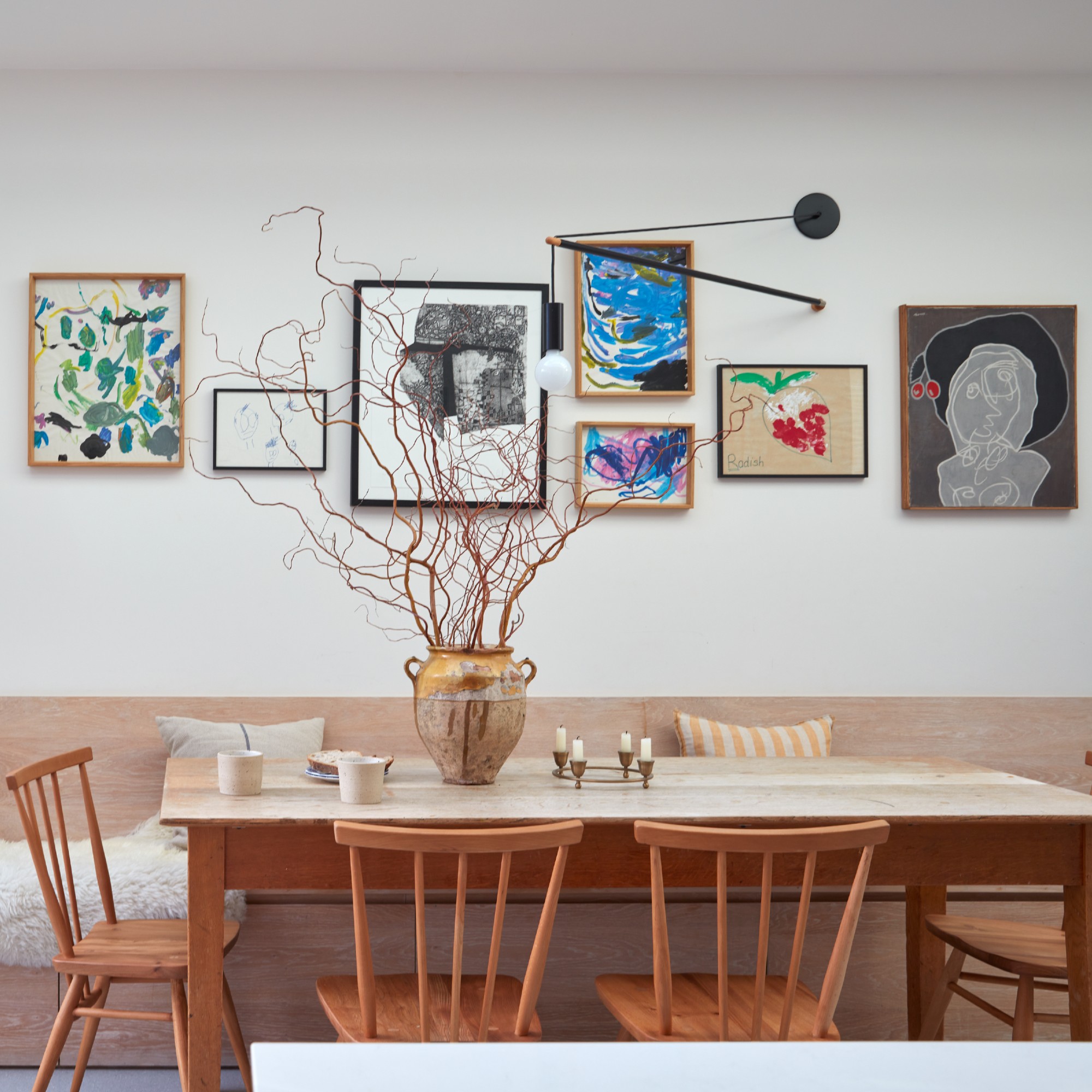 A dining area with a rectangular table, a built-in bench and a gallery wall with a sculptural wall light