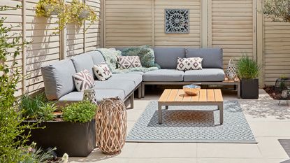 Outdoor seating area with corner sofa in front of cream painted fence