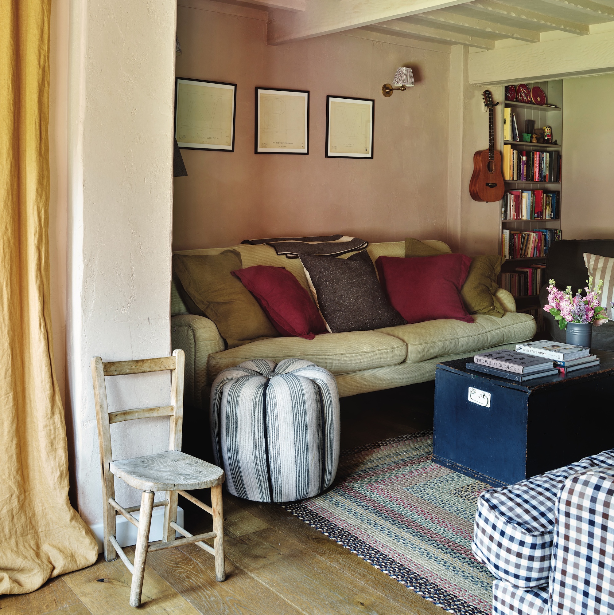 cottage living room with pink walls, cream sofa, wooden trunk used as coffee table and striped pouffe