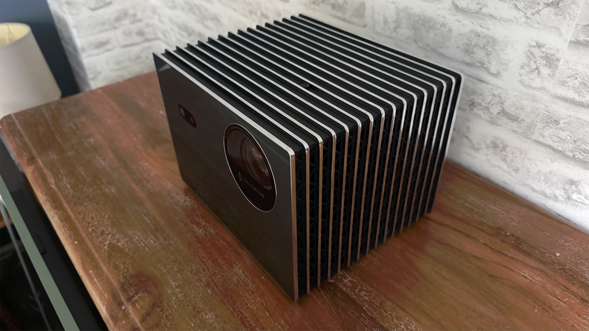 Valerion VisionMaster Pro 2 home cinema projector on wooden sideboard in front of white brick wall