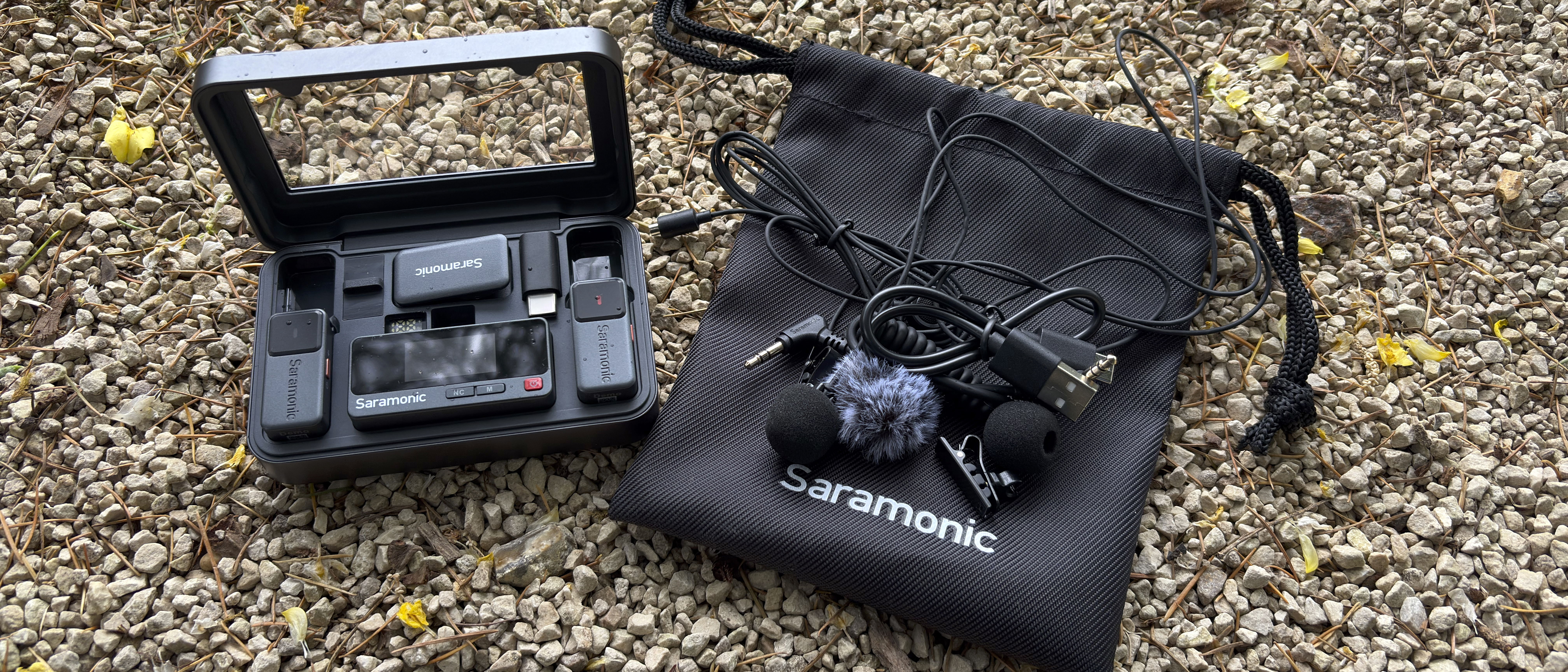 Shot of the complete kit, including the charging case holding the mics and receiver, plus a draw-string bag which holds two lavalier clip mics and wind shields