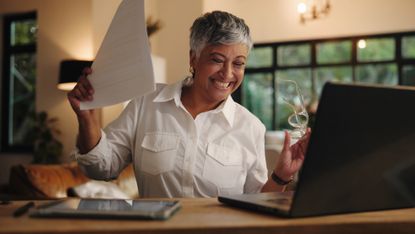 Senior woman with laptop and paperwork celebrates good news