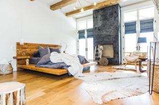 white bedroom with wooden bed, wooden floor and beams, focal fireplace, rugs on floor