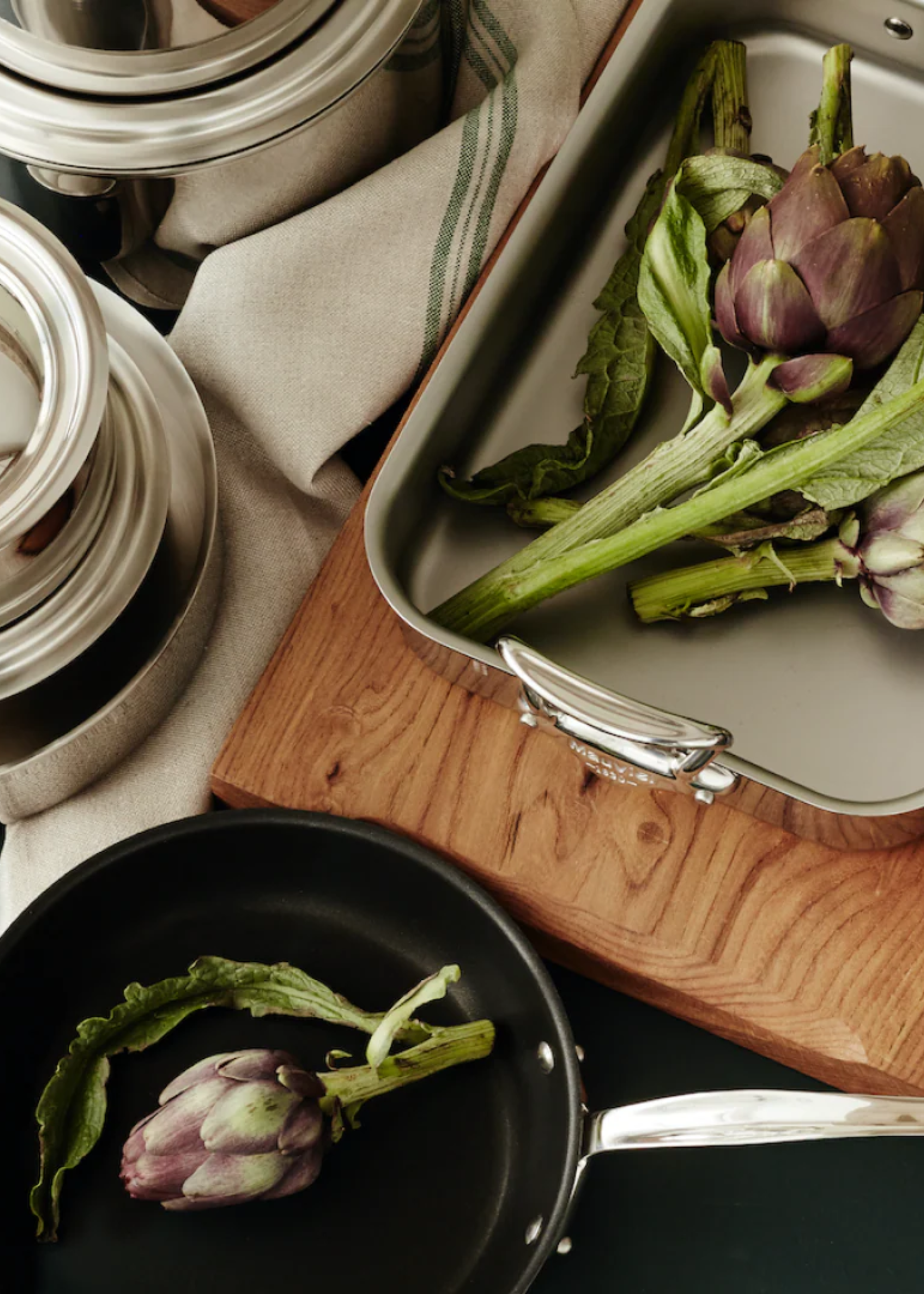 A steel baking pan and a black pan with artichokes on a kitchen countertop
