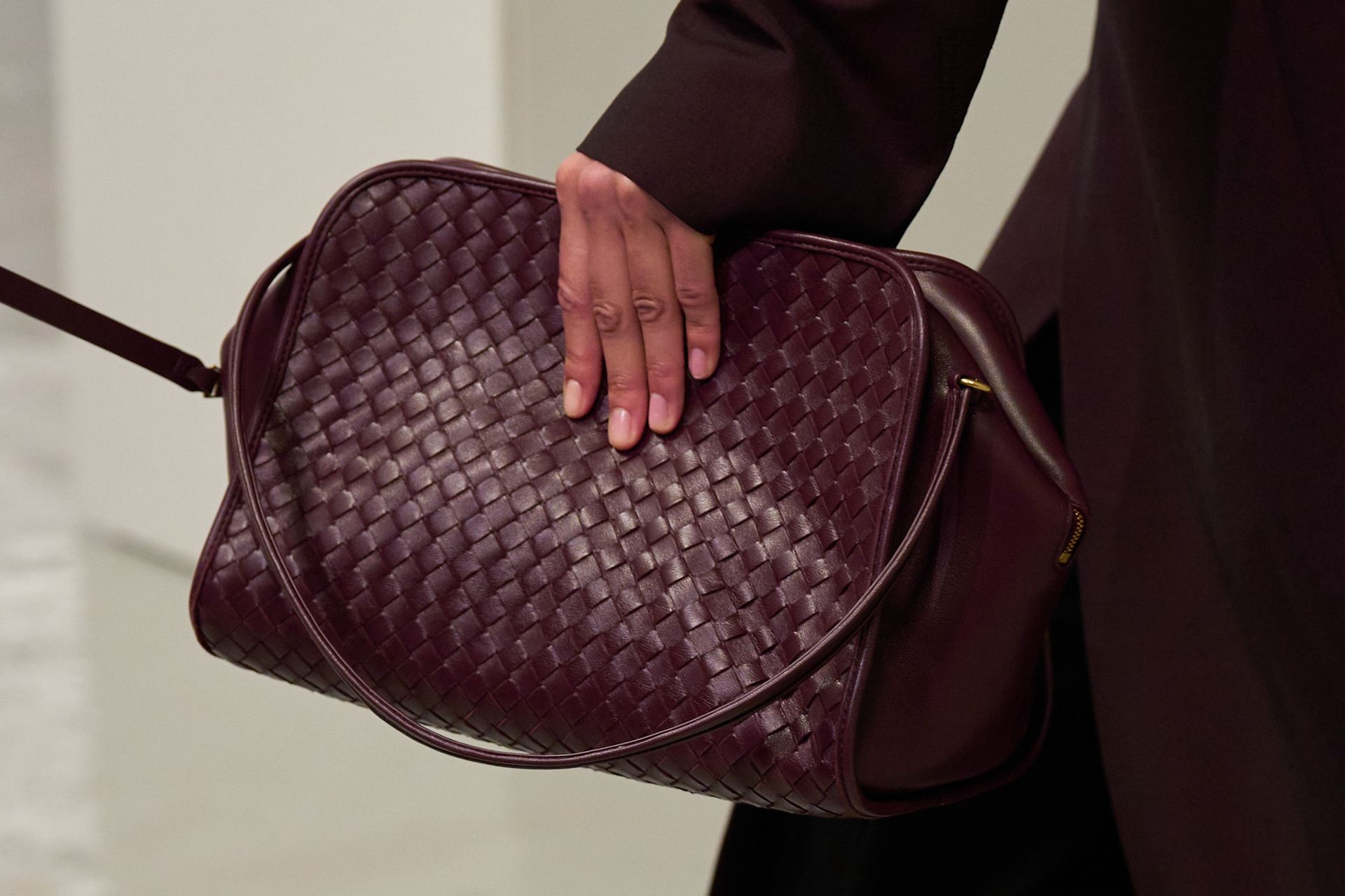 A model walking in the spring/summer 2027 Bottega Veneta show during Milan Fashion Week carrying a burgundy intrecciato shoulder handbag.