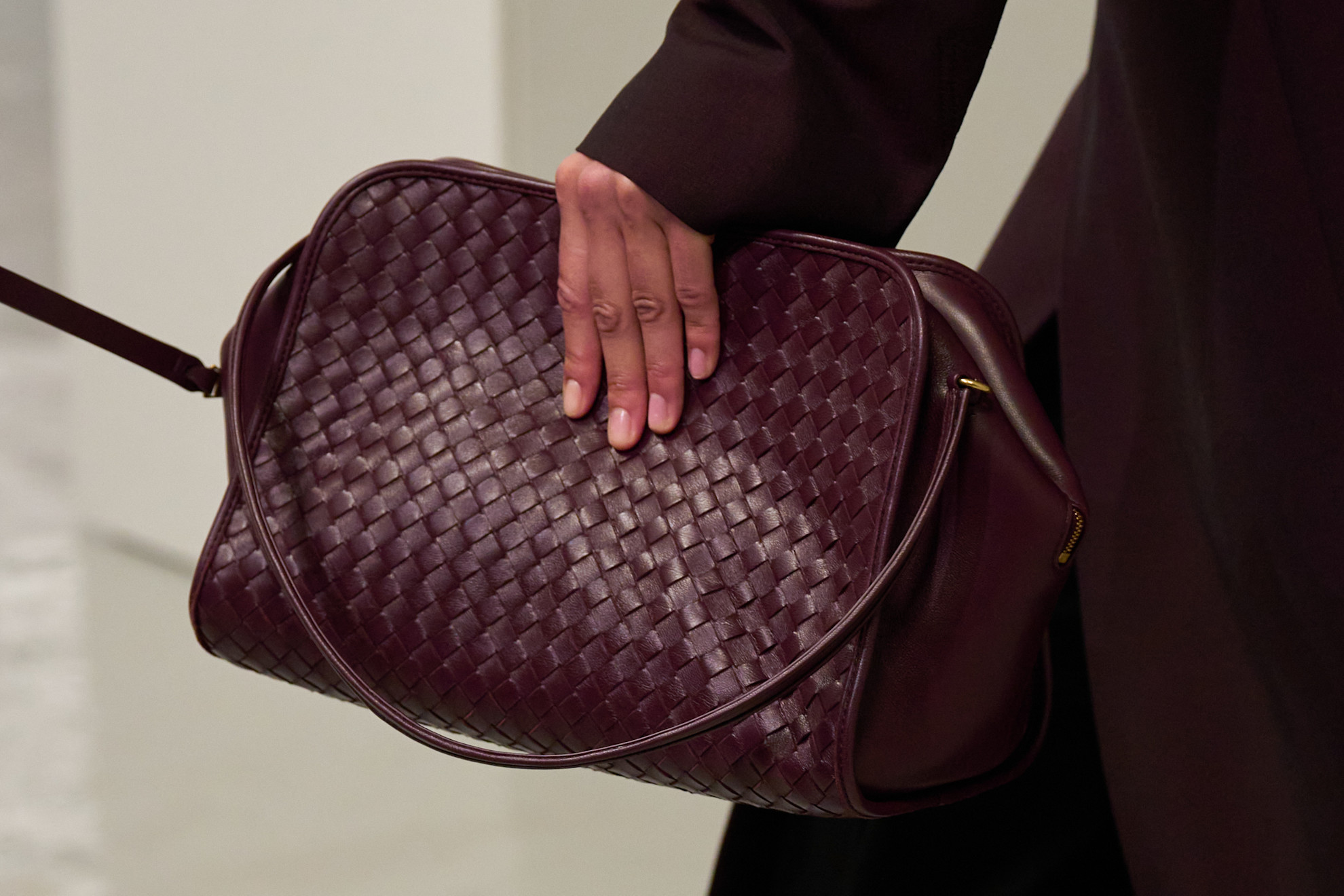 A model walking in the spring/summer 2027 Bottega Veneta show during Milan Fashion Week carrying a burgundy intrecciato shoulder handbag.