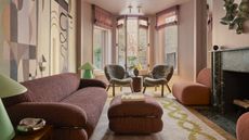 pink living room with mural on the wall, two twin armchairs in the window and green marble fireplace