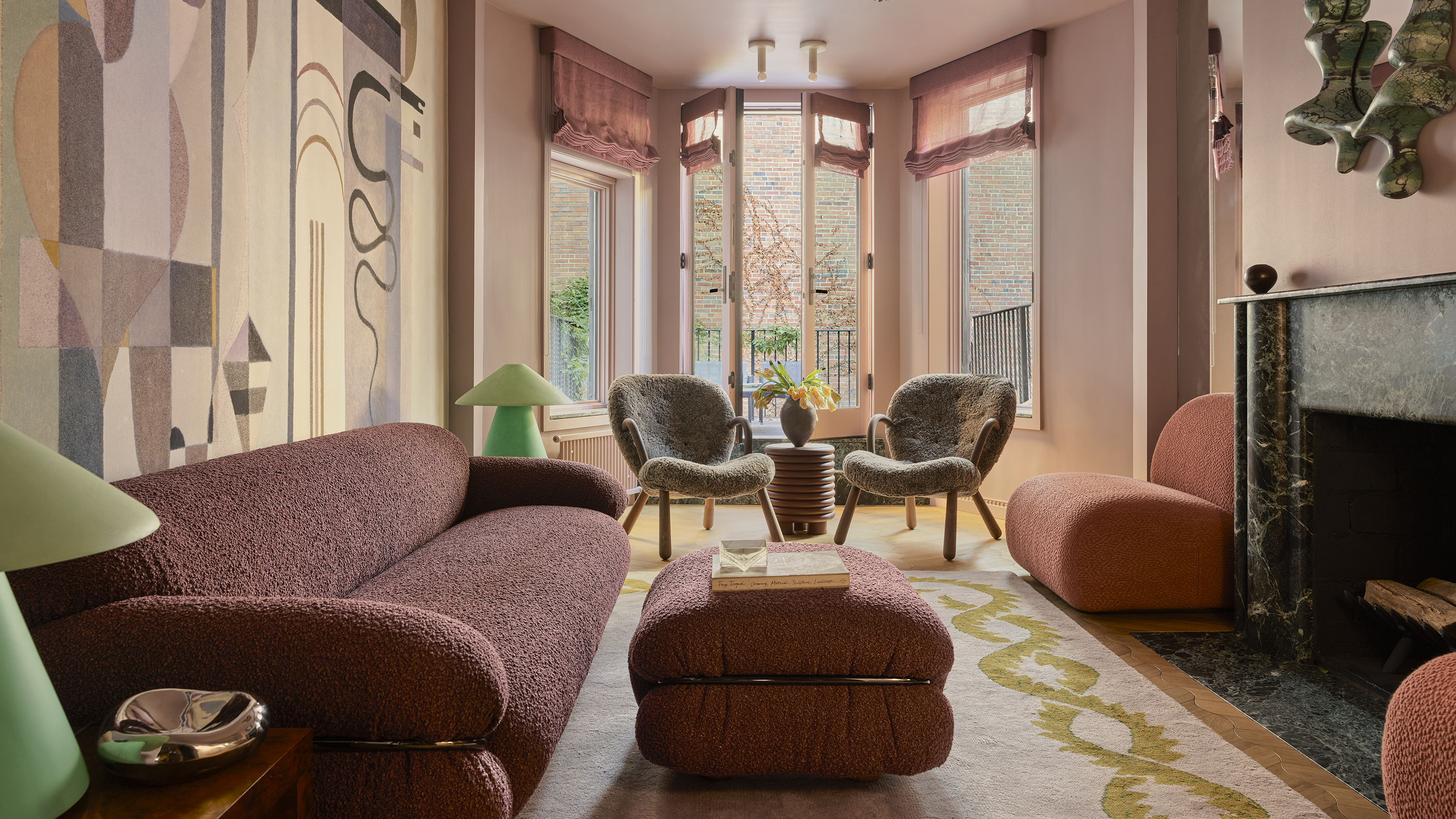 pink living room with mural on the wall, two twin armchairs in the window and green marble fireplace