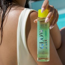 Woman in swimsuit holding up bottle of supergoop glow oil sunkissed coconut 