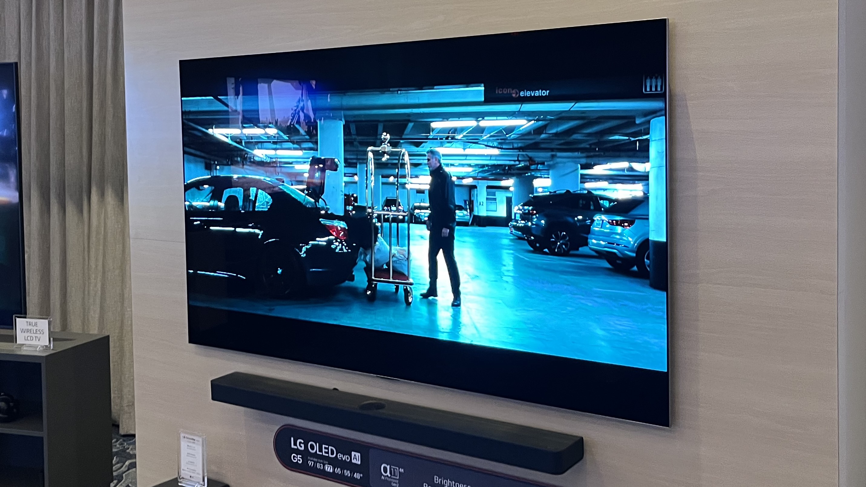 LG G5 OLED TV mounted on wall showing image of man in a parking garage