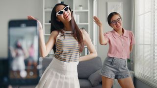  young woman with her friend tiktoker created her dancing video by smartphone camera together. To share video on social media application