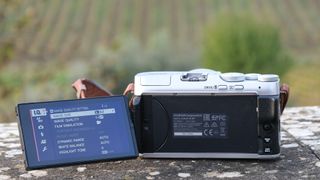 Rear of Fujifilm X-A7 with LCD screen flipped out in front of a field