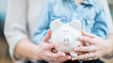 Close up of parent and child's hands holding a white piggy bank