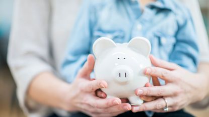 Close up of parent and child's hands holding a white piggy bank