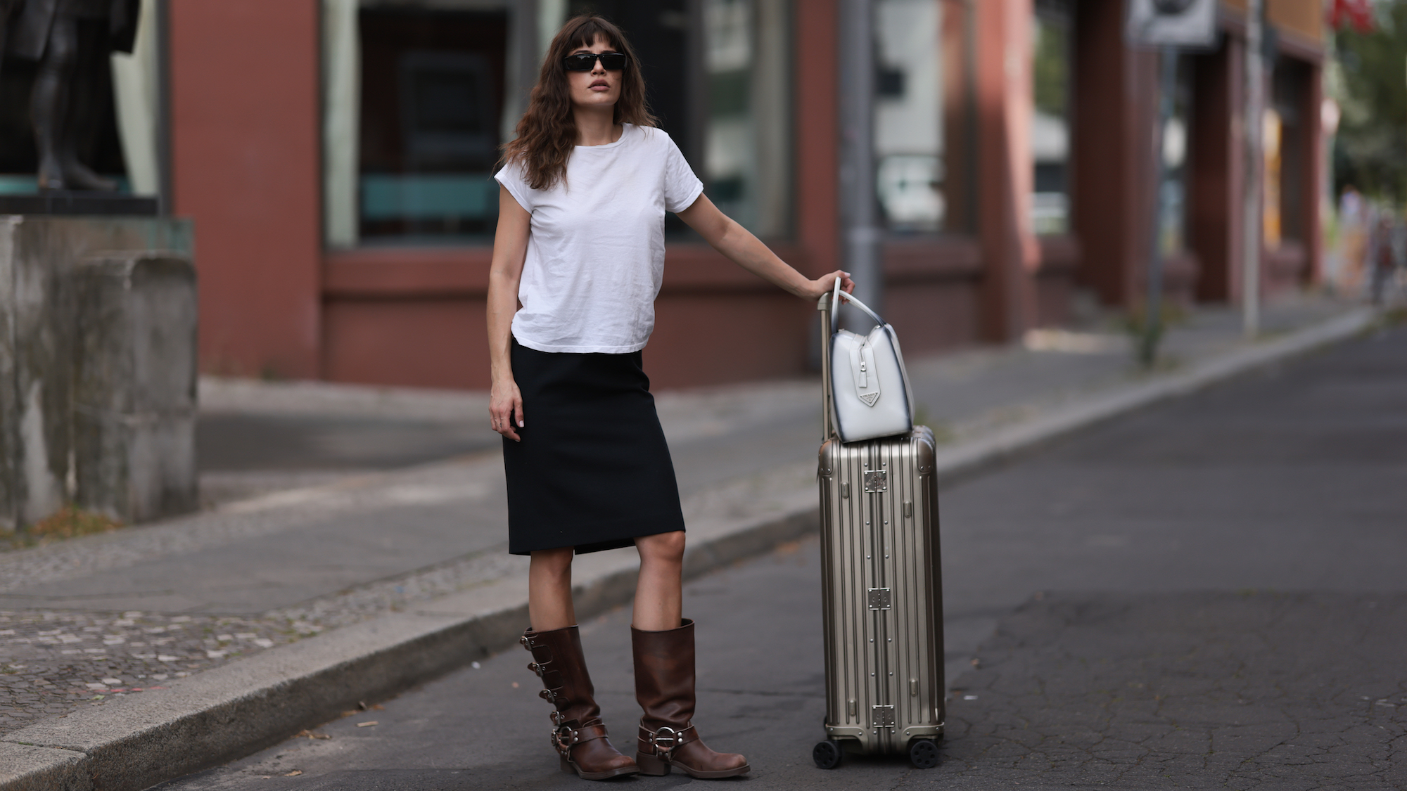 Lea Naumann wearing white tshirt, black skirt and cowboy boots with suitcase and hand luggage containing best chic miniatures