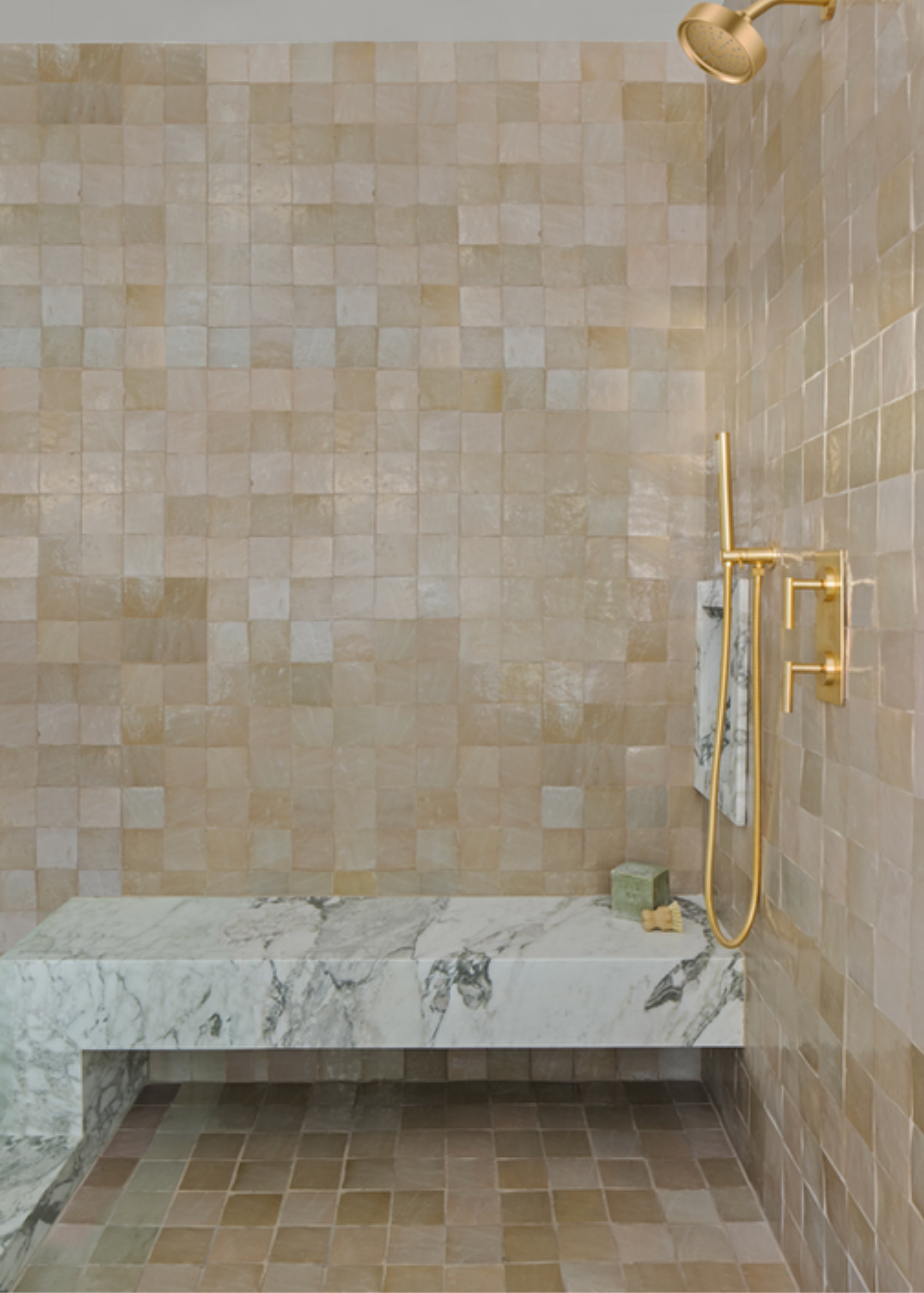 Walk in shower with floor to ceiling beige neutral zellige tiling, with a marble slab seat, and gold brassware.