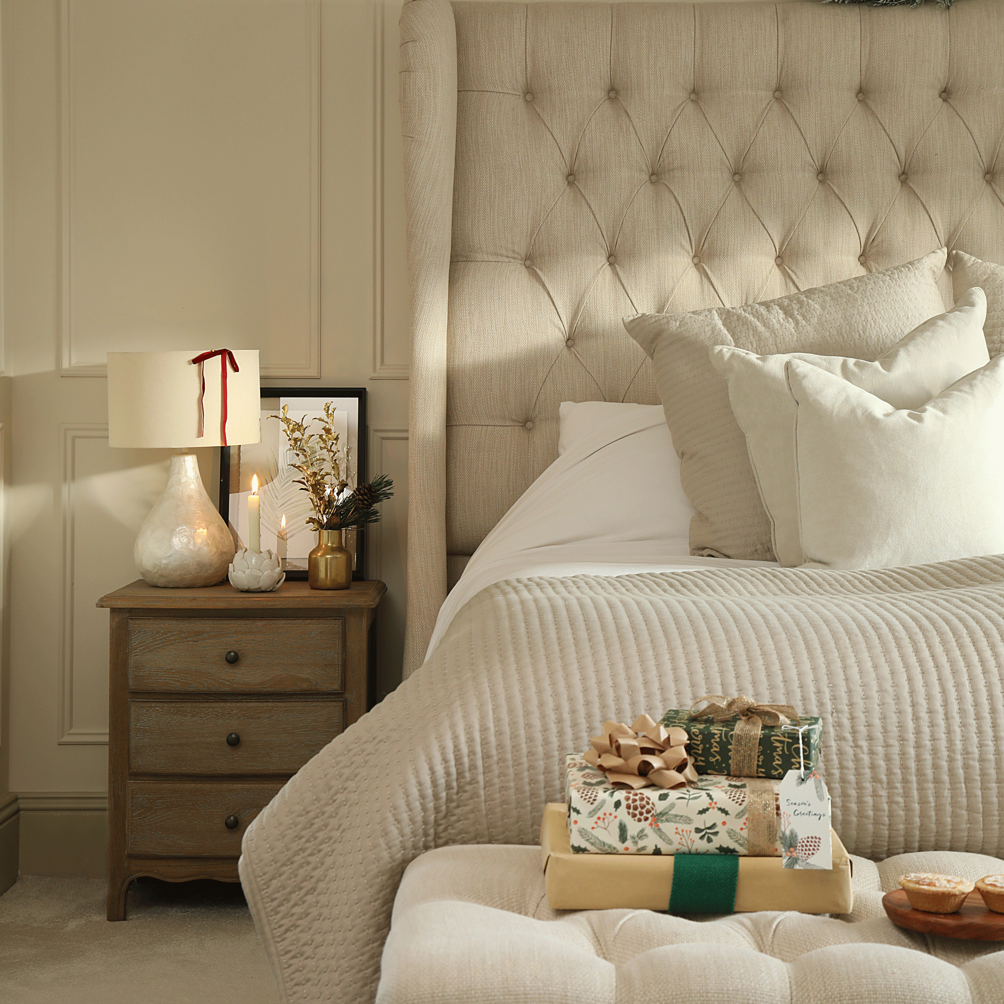 a neutral bedroom with wall panelling decorated for Christmas with presents and candles