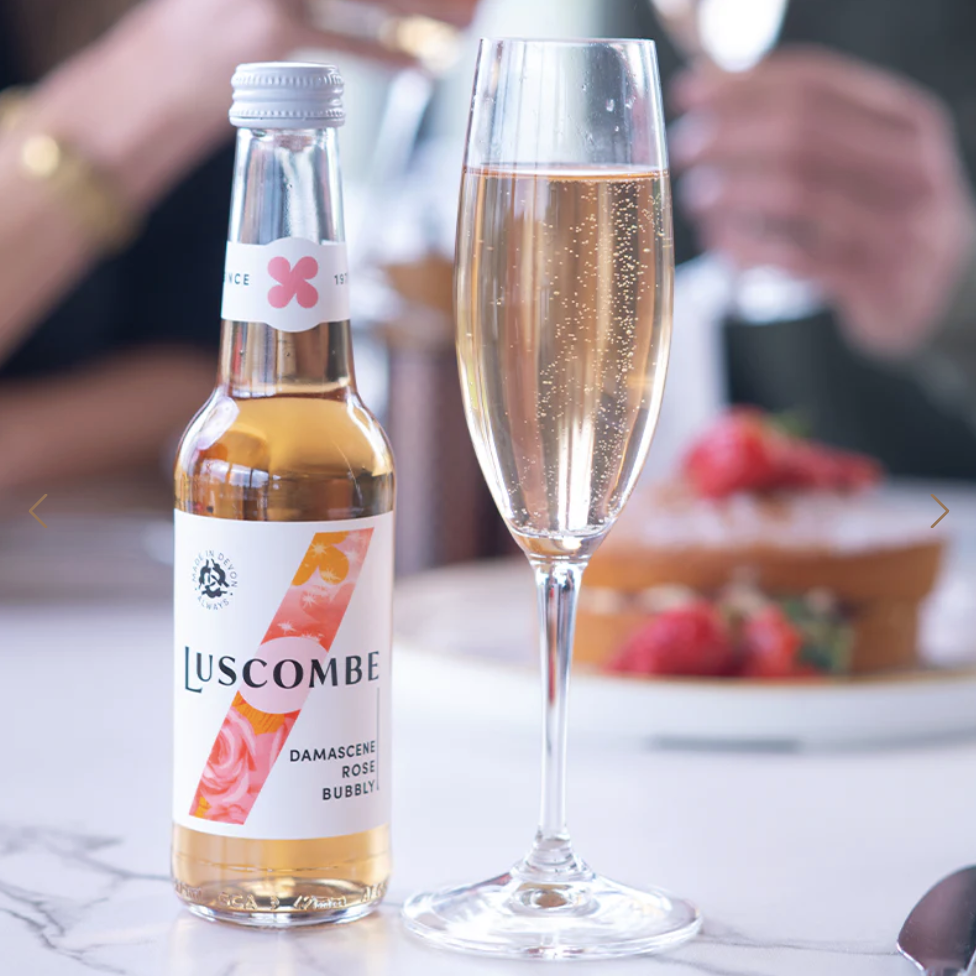 A bottle of Luscombe rose bubbly next to a glass and cake