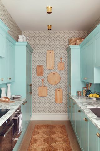 Pale aquamarine blue/green kitchen cabinets with wallpaper on walls, and wooden chopping boards decorating the wall