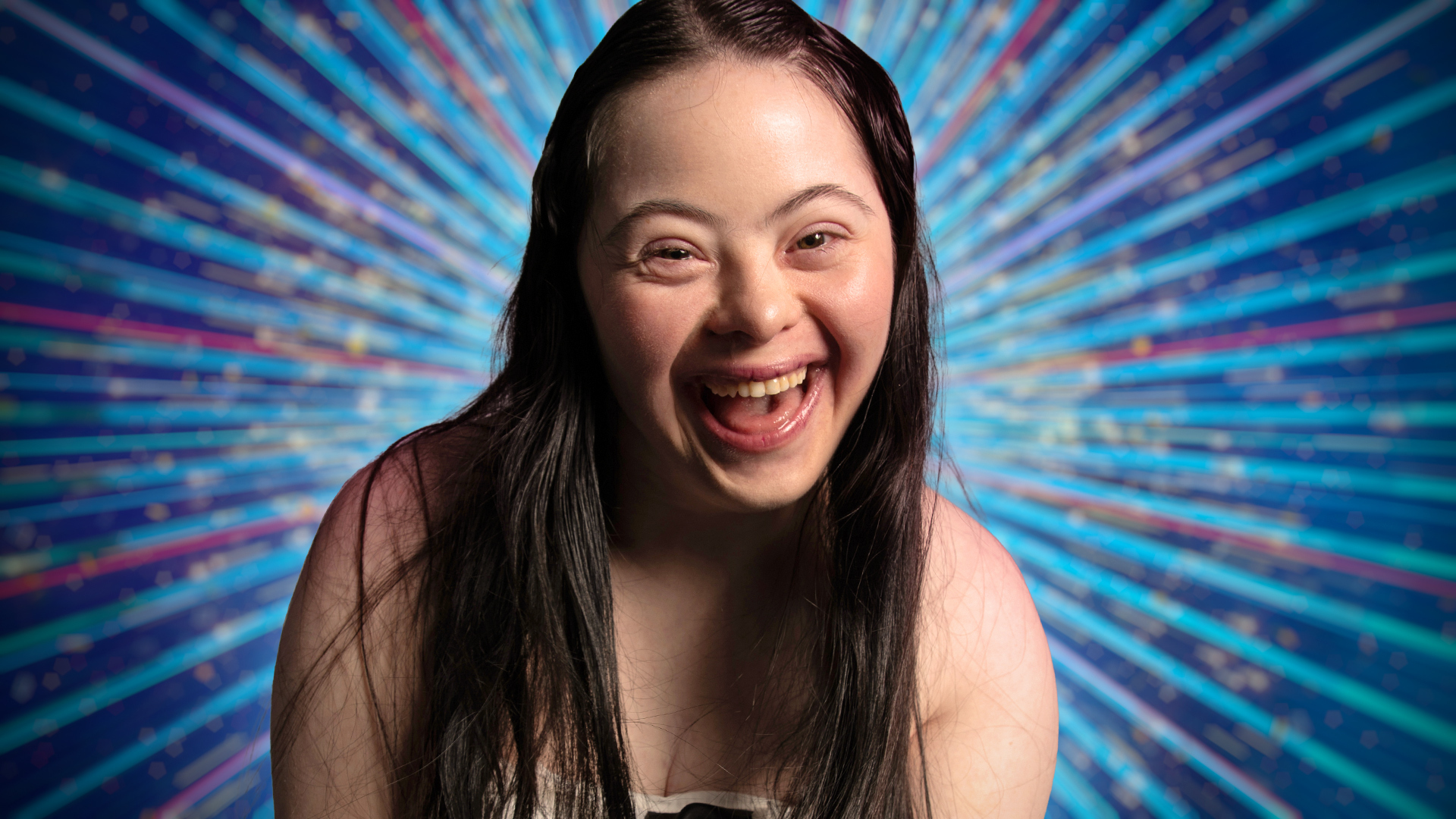 Ellie Goldstein smiling for the camera with a blue sparkly background behind her.