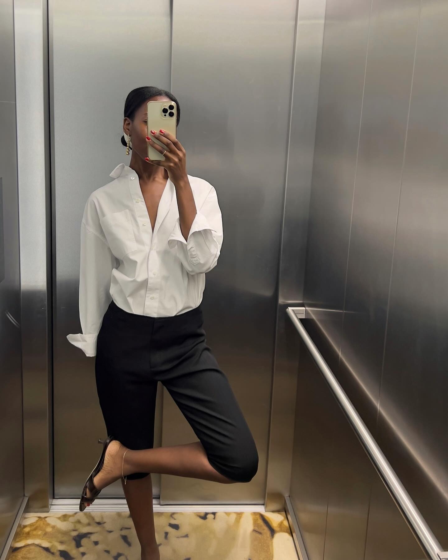 The French woman in the mirror selfie wears black capri pants, a white button down and black sandals.