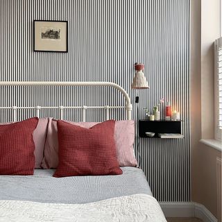 Bedroom with bed that has white metal frame and micro-stripe wallpaper.