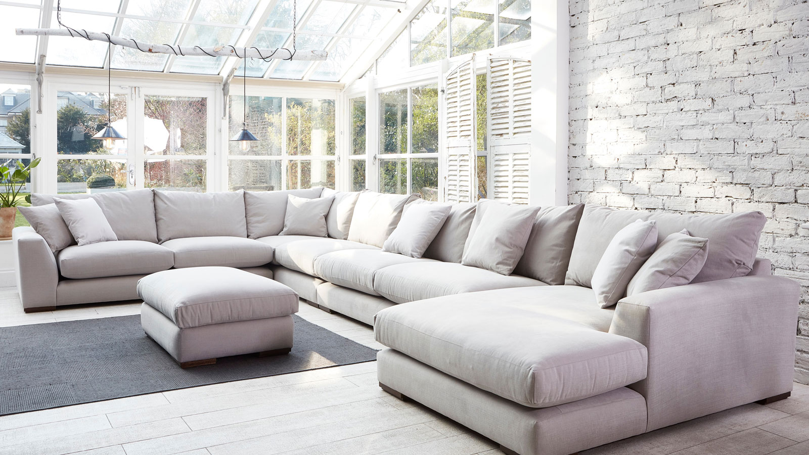 conservatory living room with large white U-shaped sofa and whitewashed exposed brick walls