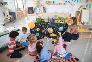 children sitting on the floor while nursery worker holds up a graphic to teach them about planets