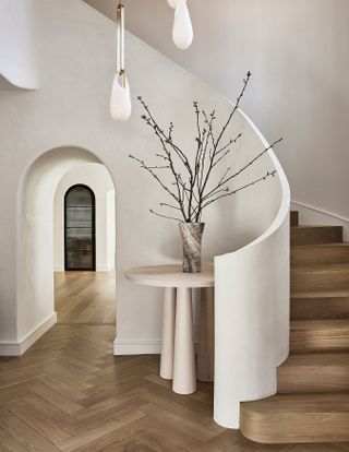 Warm, neutral entryway with round white console, wooden flooring and decorative branches
