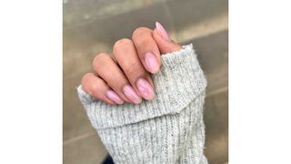 A close-up of Digital Beauty Editor, Aleesha Badkar's sheer pink almond nails/ with a pavement background