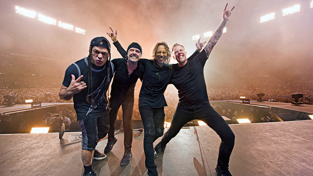 A photograph of Metallica on stage posing and throwing the horns