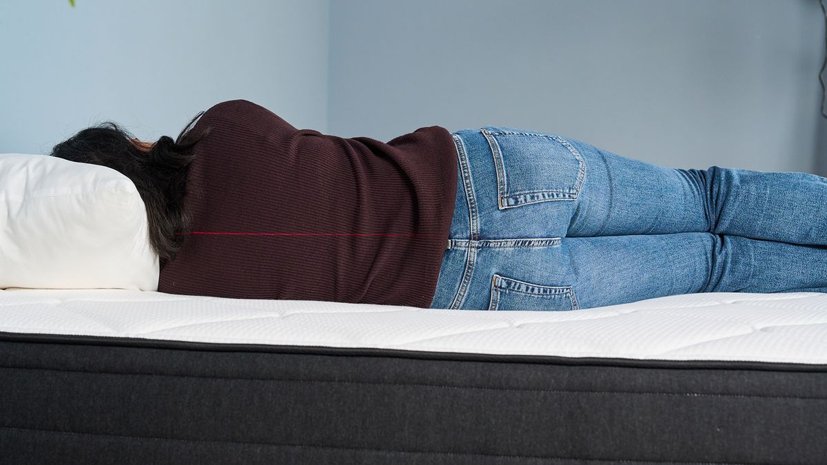Mattress tester Becky George lies on her side on the Plank Firm Luxe mattress. A red laser line runs across the middle of her body.