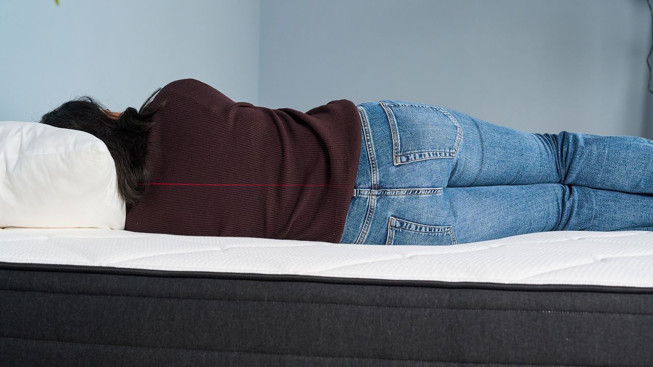 Mattress tester Becky George lies on her side on the Plank Firm Luxe mattress. A red laser line runs across the middle of her body.