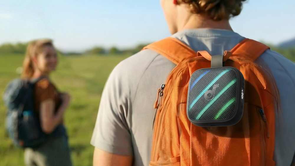 The Anker Soundcore Boom Go 3i attached to a man's backpack as he walks through a field.