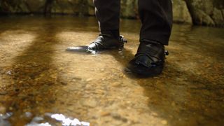 A person wearing black hiking shoes standing in a riverbed