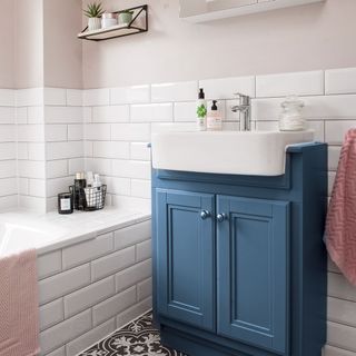 a bathroom with top half of wall in blush pink paint and bottom half with white tiles, white tile inbuilt bath, and a blue undersink cabinet